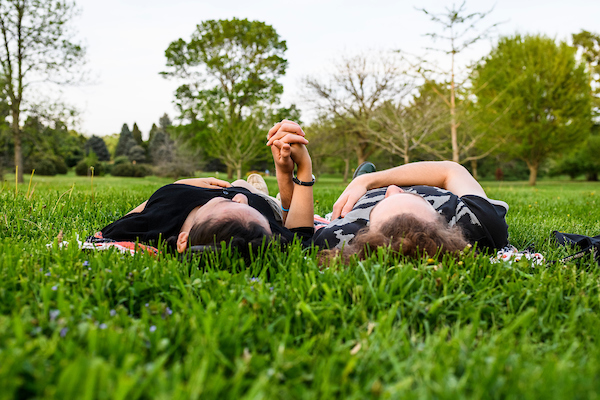 Two students lie in the grass holding hands among the flowering trees and fresh blossoms at the Longenecker Horticulture Gardens.
